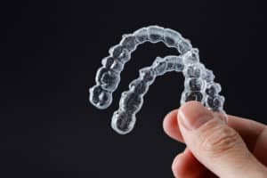 invisalign vs. braces - a hand holding a pair of Invisalign clear teeth aligners